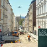 Blick auf die Neue Norsdstraße, die komplette Baustelle ist. Im Vordergrund steht leicht unscharf ein Notizbuch mit der Aufschrift »LOGBUCH« auf dem Mauer-Sims.