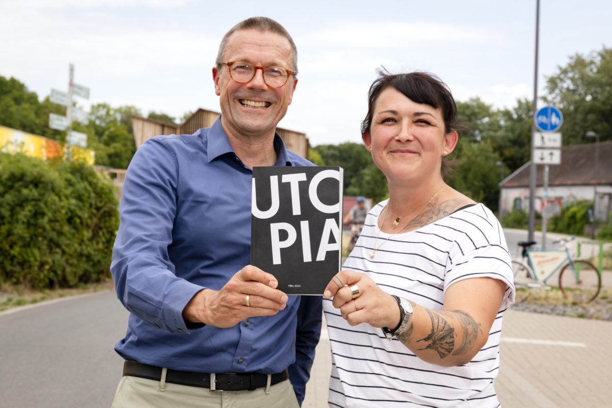 Uwe Schneidewind und Beate Blaschczok halten die Utopiastadt Fibel in die Kamera