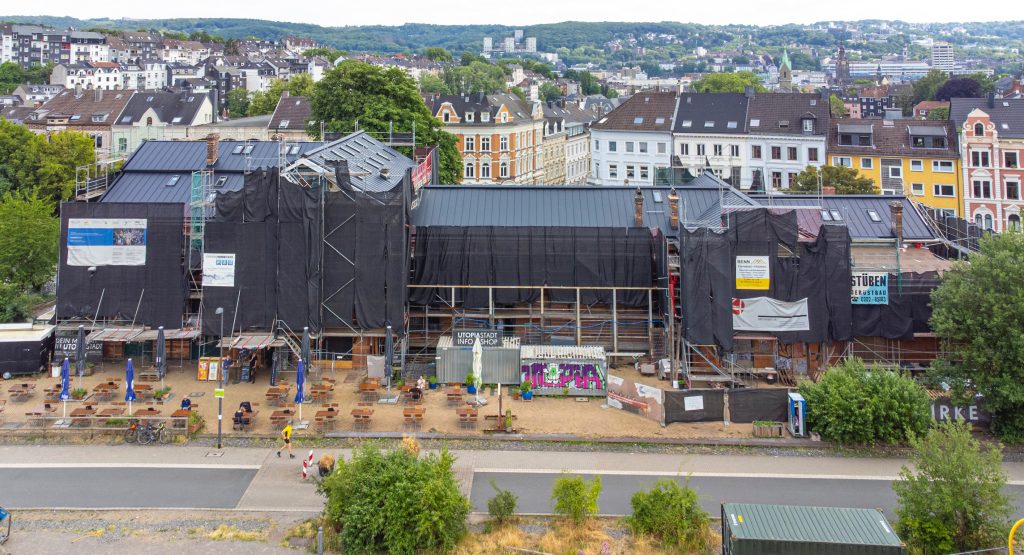 Blick von schräg aus nördlicher Richtung oben auf das eingerüstete Bahnhofsgebäude mit schickem neuen Dach.