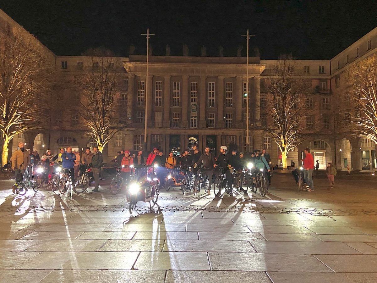 Rathausvorplats im Dunkeln, viele Menschen auf Fahrrädern mit eingeschaltetern Radbeleuchtung Richtung Kamera