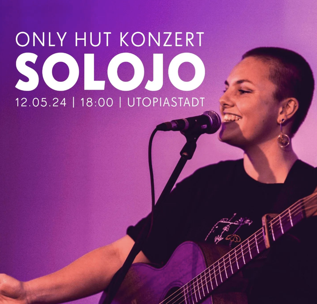 Solojo lachten am Mikrofon mit umgehängter Gitarre | Only Hut-Konzertankündigung Utopiastadt 12.5.24